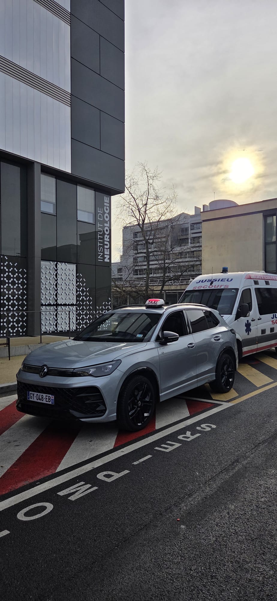 Taxi SUV gris stationné près d’un bâtiment et d’une ambulance.